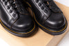 Pair of black leather shoes with yellow stitching on a cardboard surface