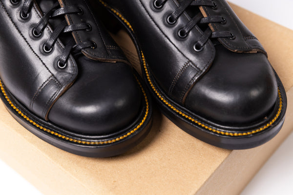 Pair of black leather shoes with yellow stitching on a cardboard surface