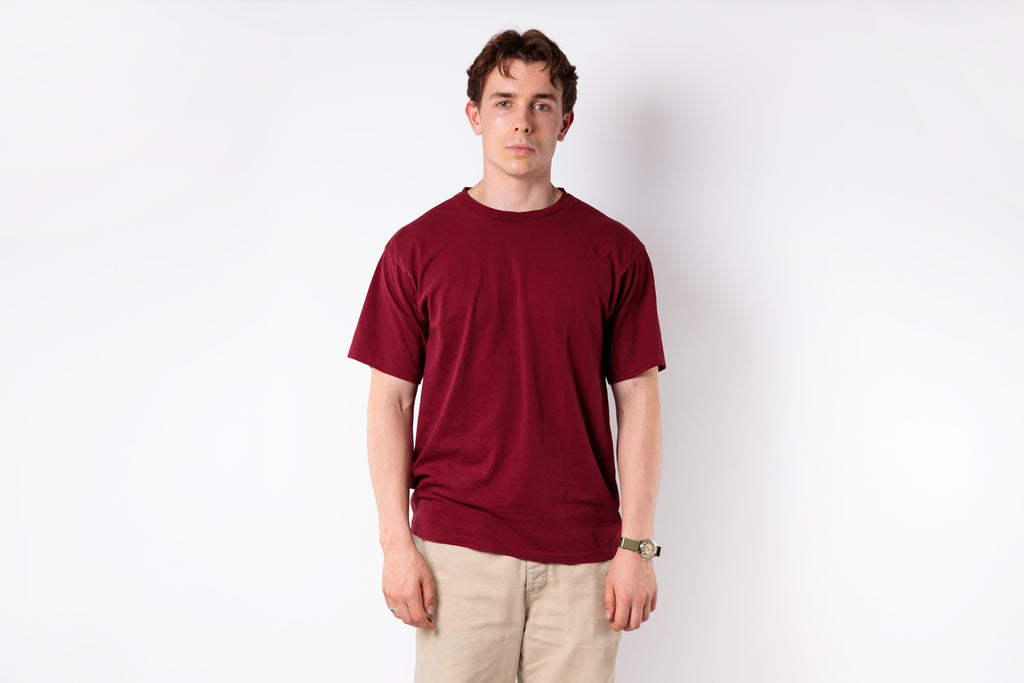 Man wearing a red t-shirt and beige pants against a white background
