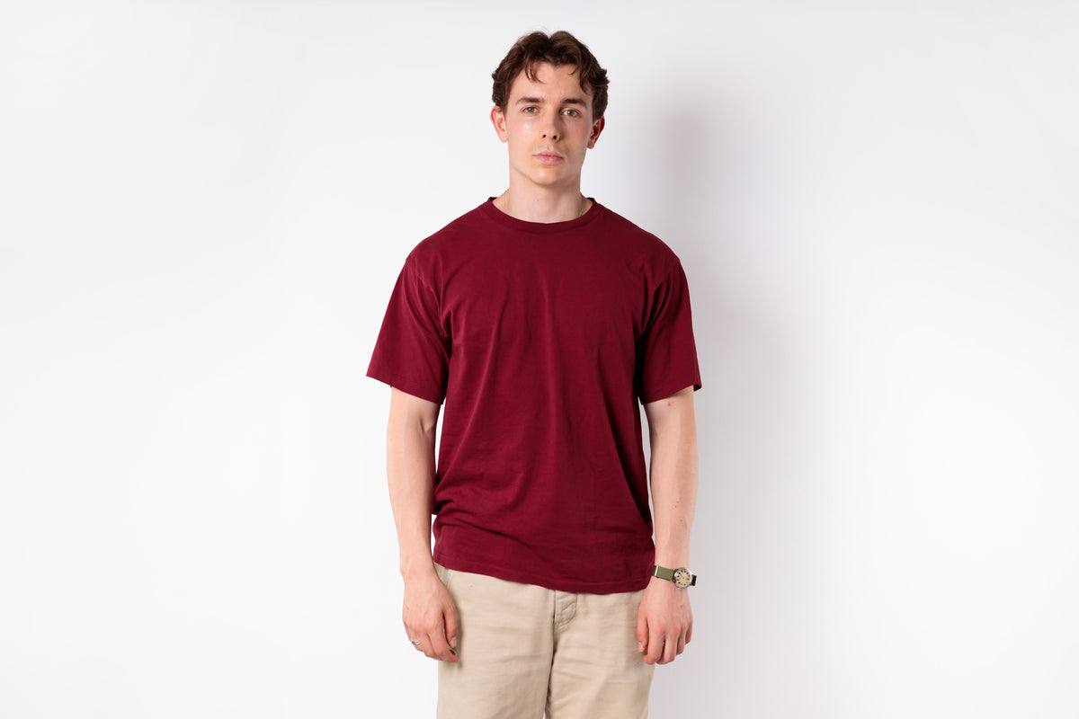 Man wearing a red t-shirt and beige pants against a white background