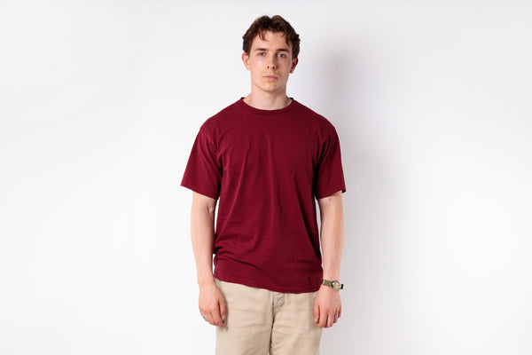 Man wearing a red t-shirt and beige pants against a white background