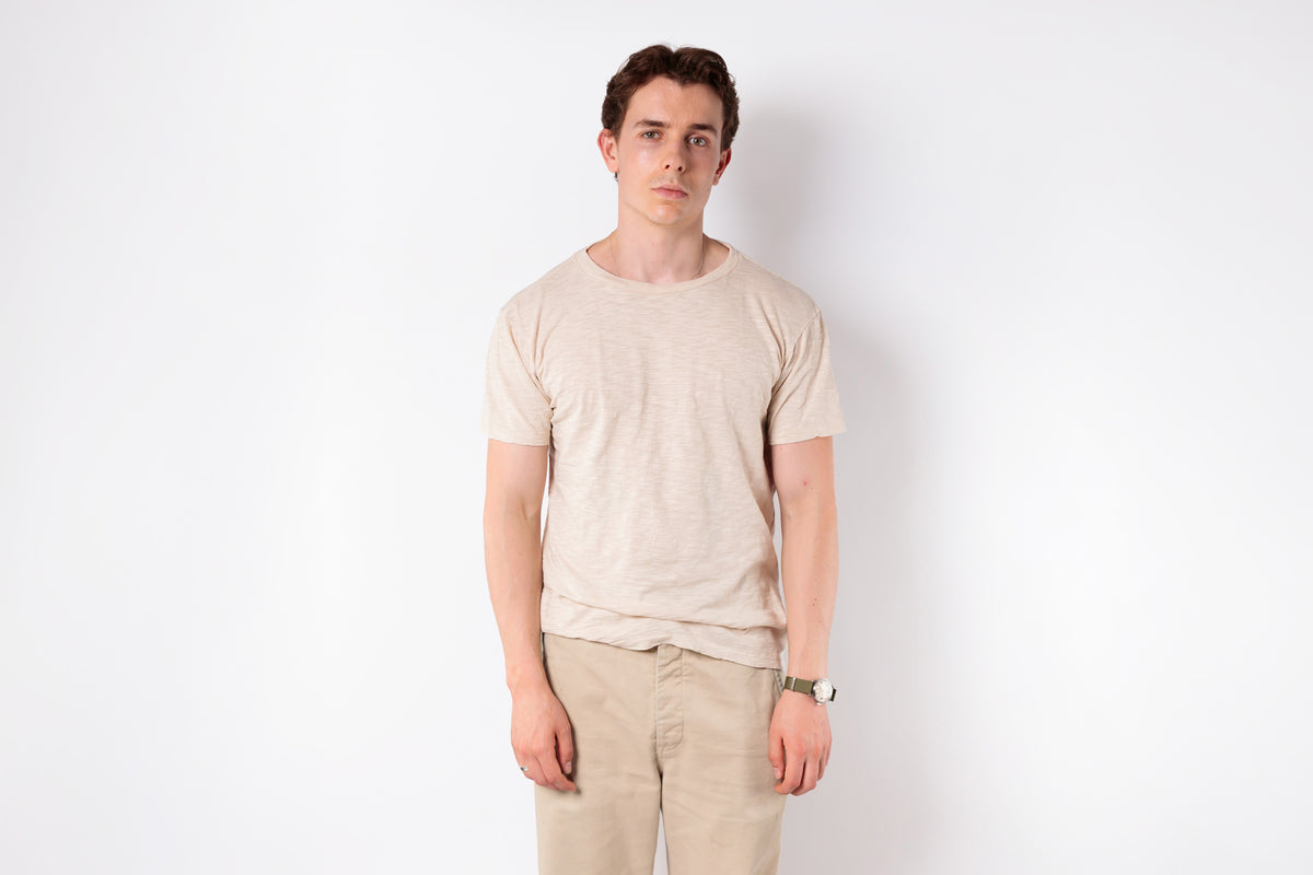 Man wearing a beige t-shirt and pants against a white background