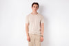 Man wearing a beige t-shirt and pants against a white background