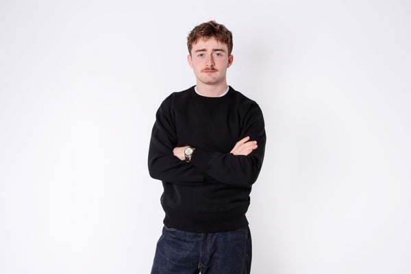 Man wearing a black sweater and dark pants against a white background