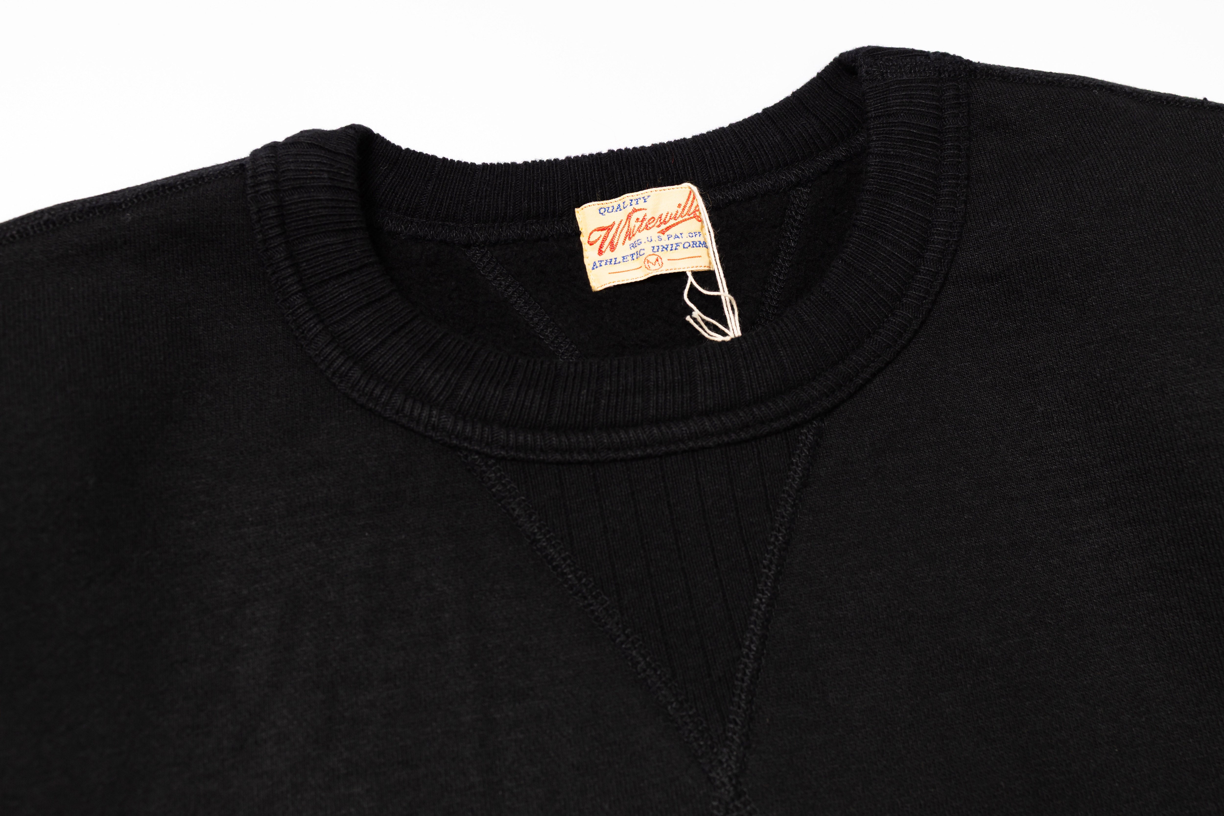 Close-up of a black sweater with a brand tag on a white background