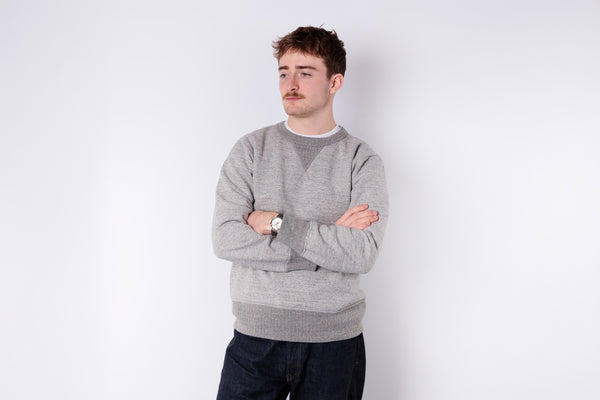 Man wearing a gray sweater and black pants against a white background