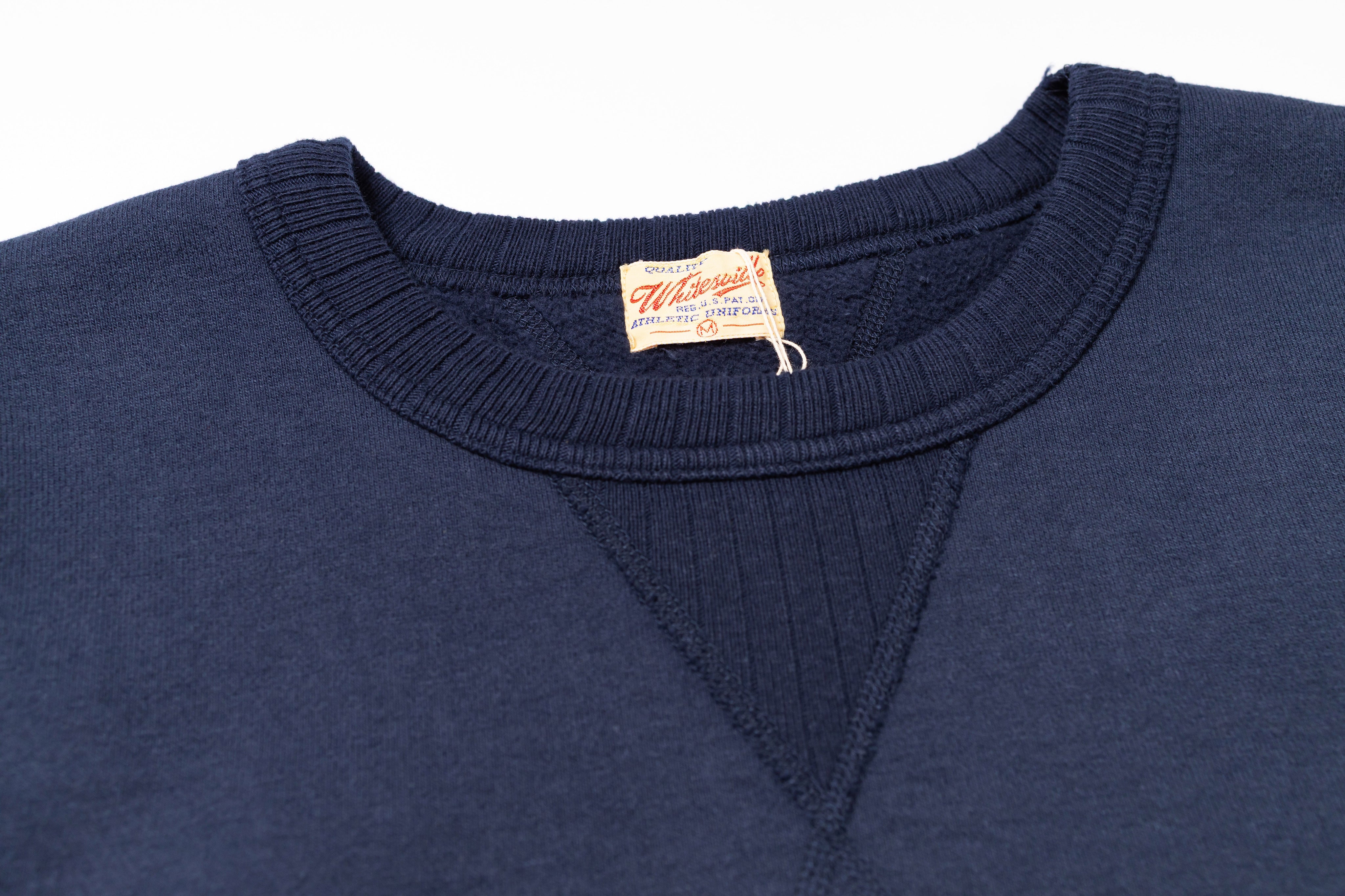 Close-up of a navy blue sweater with a brand label on the collar against a white background