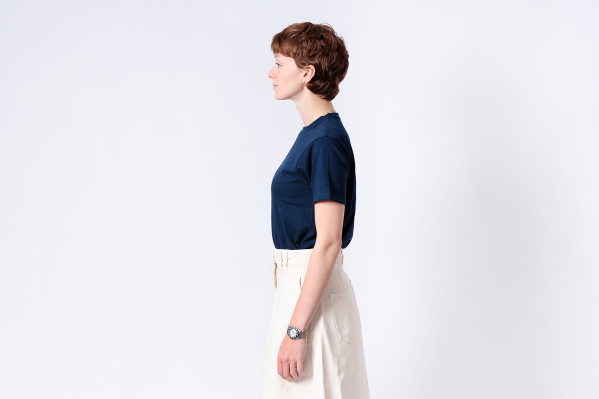Person wearing a navy blue shirt and white pants on a light gray background