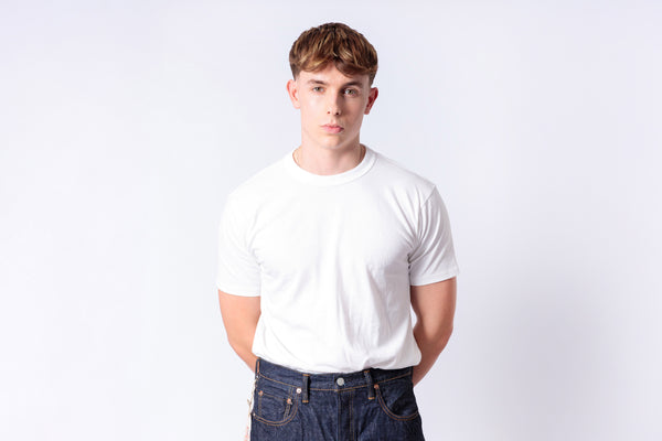 Person wearing a plain white t-shirt and dark jeans on a light gray background