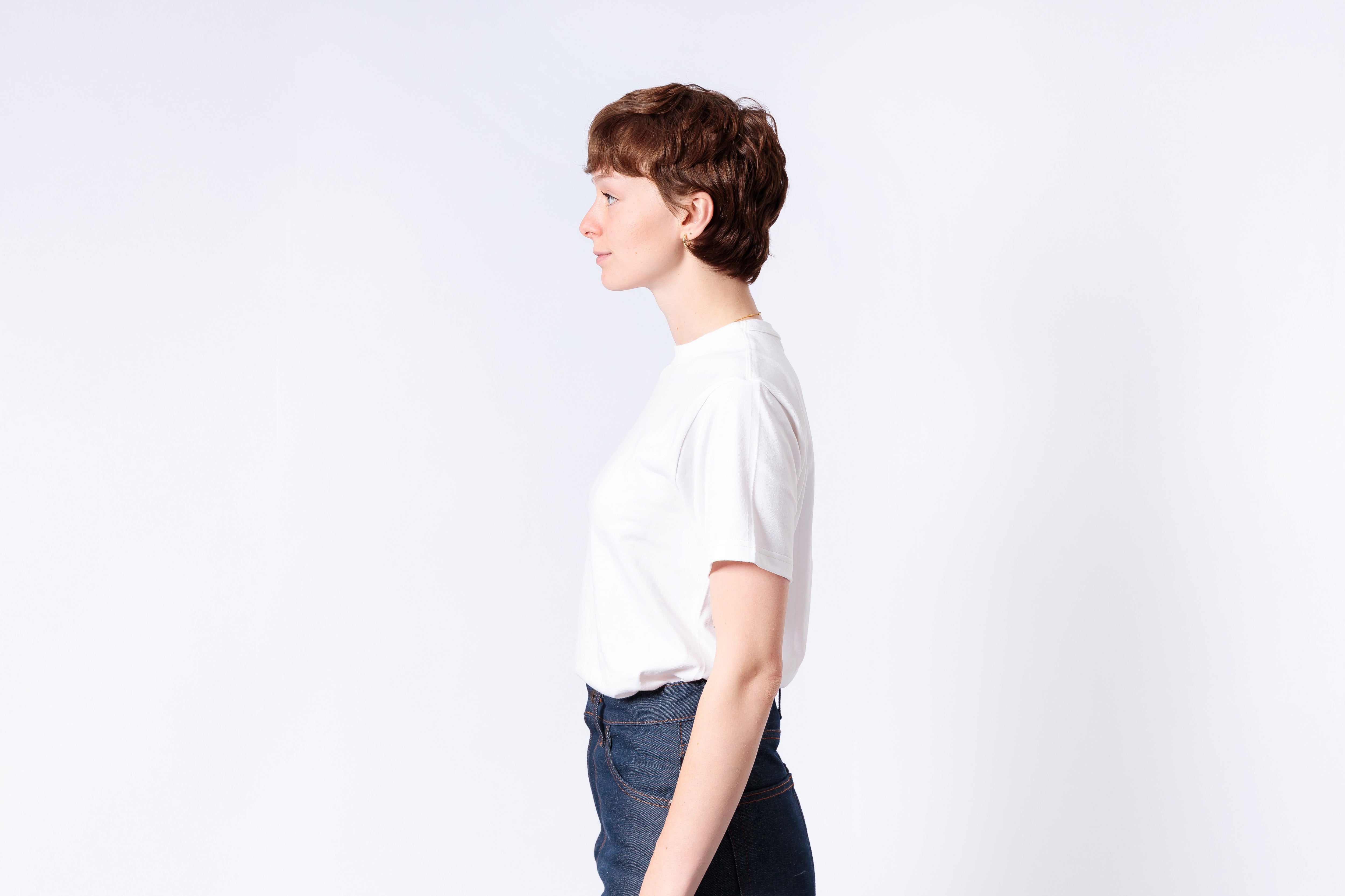 Person wearing a white t-shirt and dark pants on a light gray background