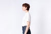 Person wearing a white t-shirt and dark pants on a light gray background